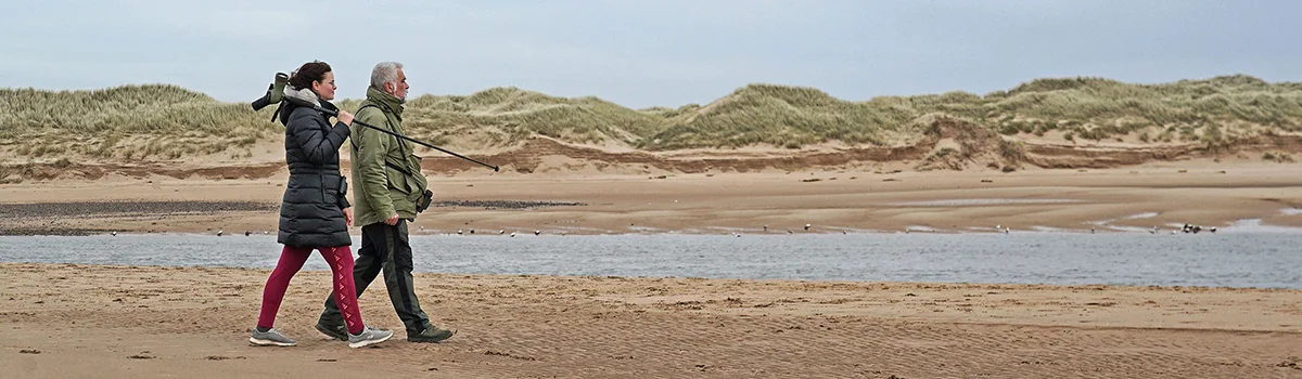 Couple walking on the beach using Kowa binoculars